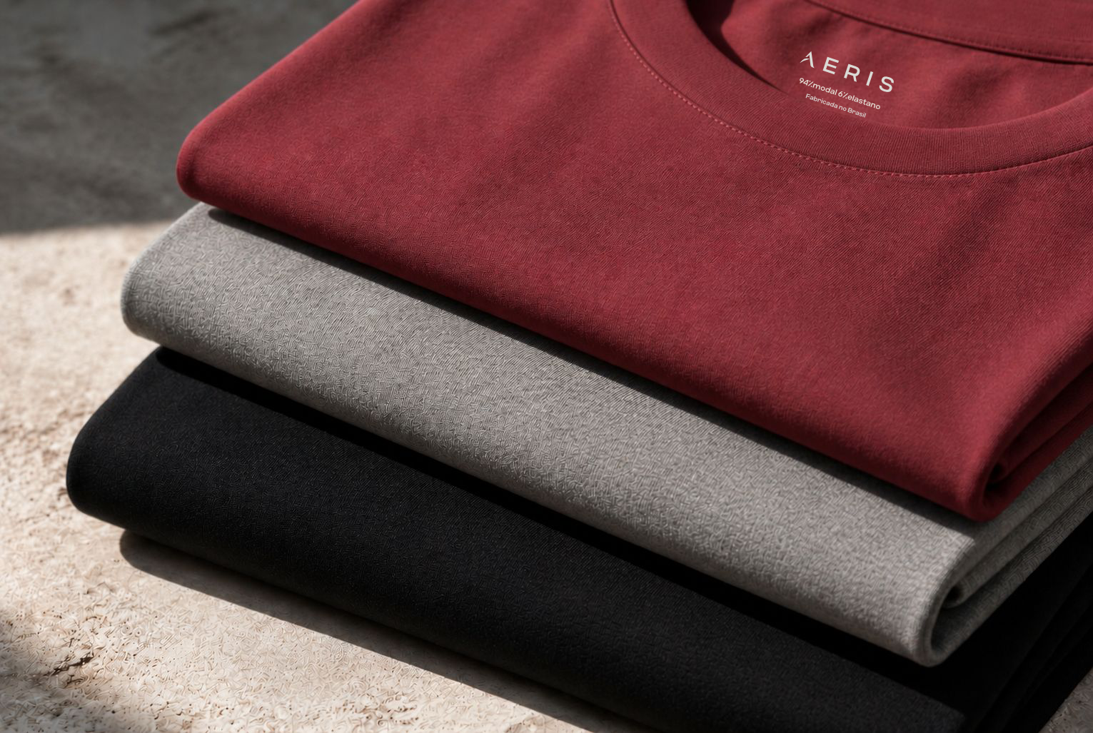 Camisetas Aeris dobradas em tons vinho, cinza e preto